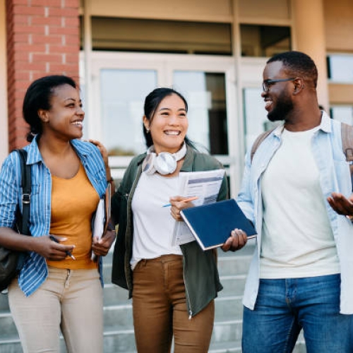 Happy multi-ethnic college friends having fun after the lecture and communicating while walking at campus.